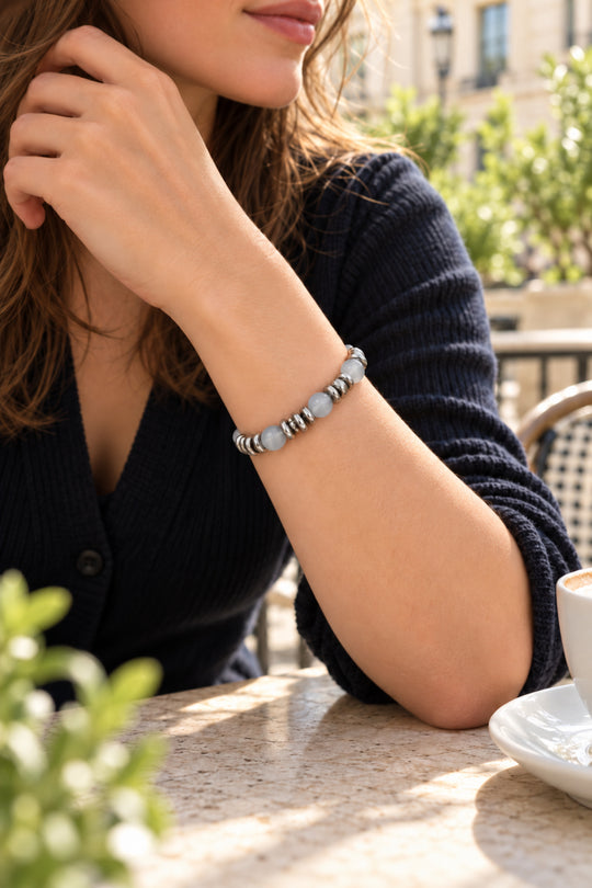 Nahaufnahme des getragenen APAERZ SELENA Armbands mit grauen Katzenaugensteinen in einer Café-Szene im Freien